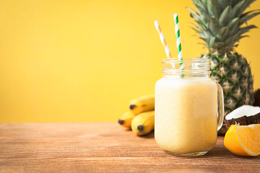 Fresh exotic smoothie with fruits and coconut milk on yellow background. Copy space.