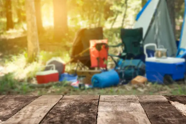 Photo of Empty, wooden table in forest with camping scene in background.