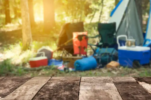 Empty, rustic wooden table in a forest area with camping scene in the background.  No people.