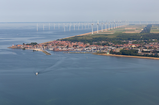 Aerial view Dutch fishing village with harbor and big offshore wind turbines along the coast