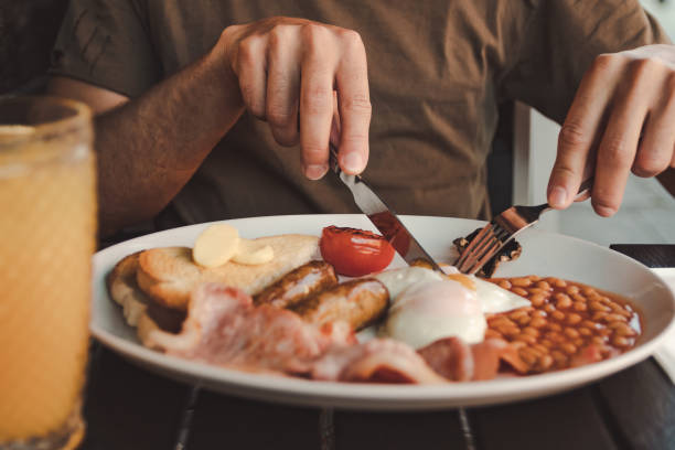 close up of a plate of english breakfast man eating an english breakfast with orange juice on a black table english breakfast stock pictures, royalty-free photos & images