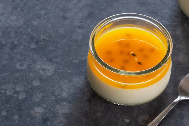 Tropical passionfruit panna cotta, an Italian pudding made from milk and cream. This dessert is topped with a layer of passion fruit gelatin, with copy space on the left side of the image.