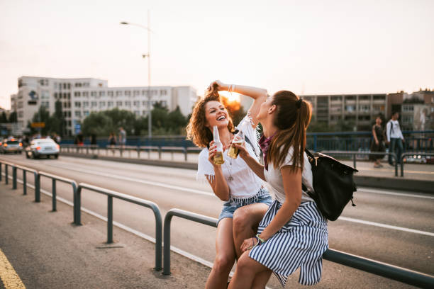 istock Two girls laughing and drinking on the bridge. 1019597740