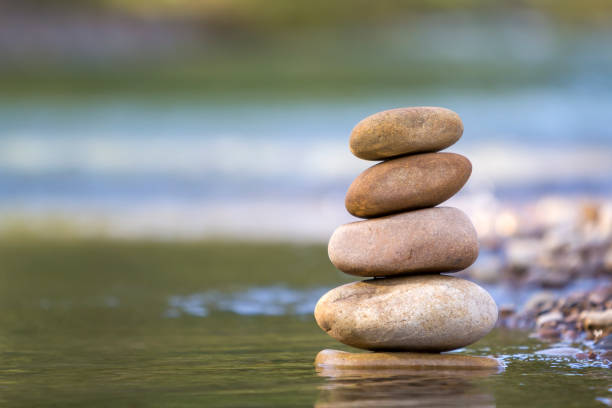 istock Close-up abstract image of wet rough natural brown uneven different sizes and forms stones balanced like pyramid pile landmark in shallow water on blurred blue-green misty copy space background. 1019607758