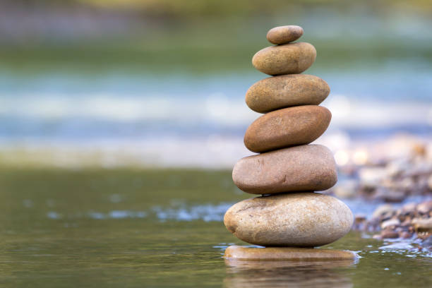 istock Close-up abstract image of wet rough natural brown uneven different sizes and forms stones balanced like pyramid pile landmark in shallow water on blurred blue-green misty copy space background. 1019607816