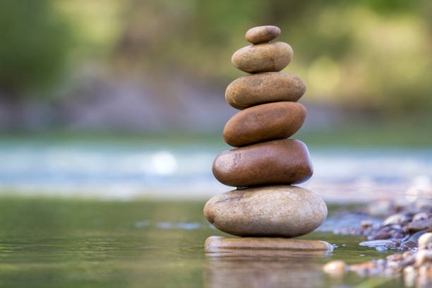 istock Close-up abstract image of wet rough natural brown uneven different sizes and forms stones balanced like pyramid pile landmark in shallow water on blurred blue-green misty copy space background. 1019607854