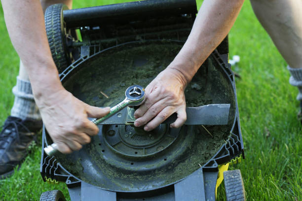 DIY Replacing a Lawn Mower Blade A man uses a work tool to fasten a nut on a battery-powered lawn mower outdoors. blade stock pictures, royalty-free photos & images