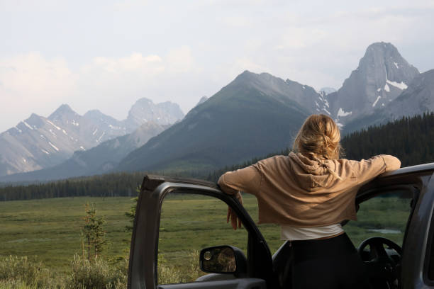 Young woman stops driving to relax and enjoy the view, mountain range behind