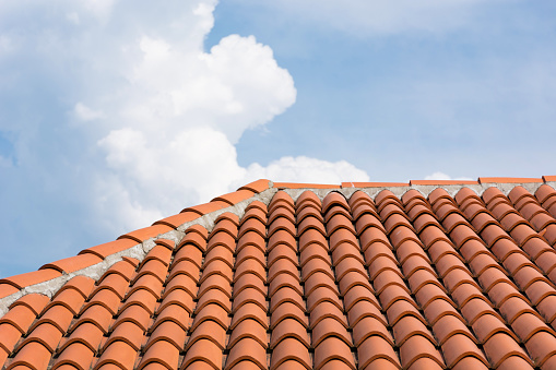 Beautiful and new orange roof tile pattern over blue and cloudy sky. Roof on modern house building. Close up
