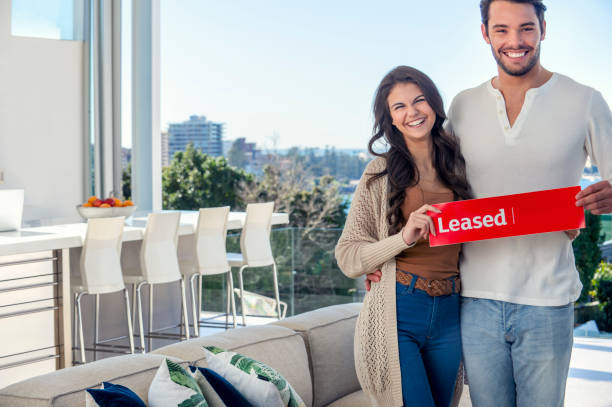 young couple holding a leased rental sign in a luxury home. - for rent sign house sign happiness imagens e fotografias de stock