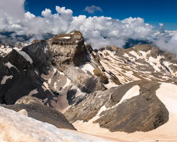 View from the summit of Monte Perdido in spanish Pyrenees. Sharp peaks, jagged clouds and lots of snow, despite the fact that the photo was taken in July, in warm, sunny weather.