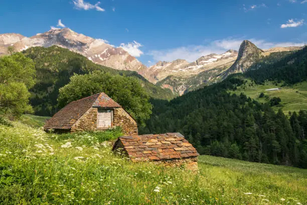 Old stone huts in a mountain valley near Viados in Pyrenees, with Pico Posets in the background. Lots of green and warm, afternoon light.