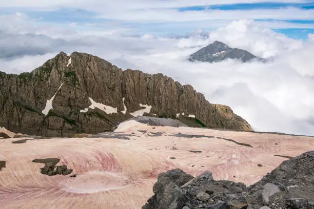 Mountain peaks protruding from the clouds, with pink glacier in the foreground. Photo taken in spanish Pyrenees.