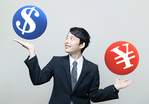 Asian businessman making comparison between a Dollar sign and a Yen (or Yuan) sign.