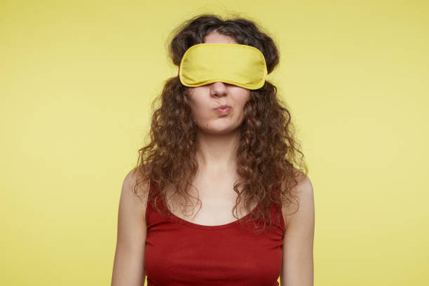 istock Puzzled irritated female curves lips, frowns face with hesitation, has clueless expression, wears yellow sleeping mask, isolated over studio wall. Woman tired of waiting for husband to come to bed. 1019737310