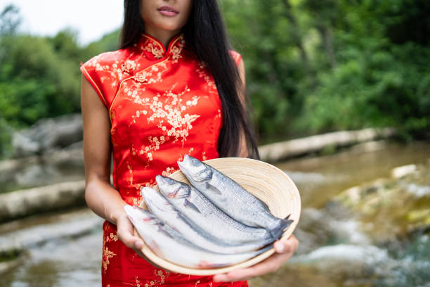 Beautiful woman in traditional chinese dress holding a basket with fish, standing in water.