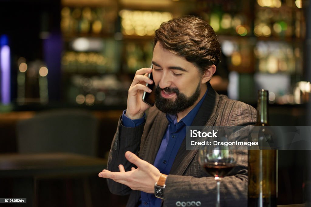 Man talking on phone Cheerful man drinking wine in restaurant and calling on phone Adult Stock Photo