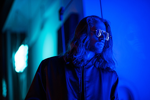 handsome young man in sunglasses under blue light on street at night