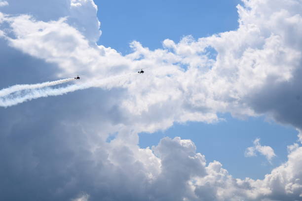 istock Two small helicopters with their rotors on flying through the sky while emmiting a lot of smoke while flying below cloudy summer sky seen during one of trips in Poland 1019842486