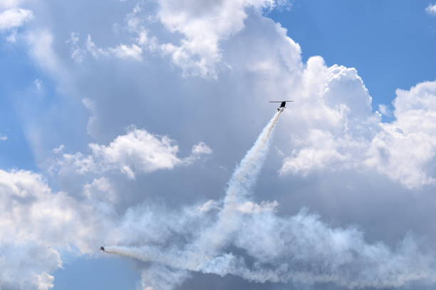 istock Two small helicopters with their rotors on flying through the sky while emmiting a lot of smoke while flying below cloudy summer sky seen during one of trips in Poland 1019845444