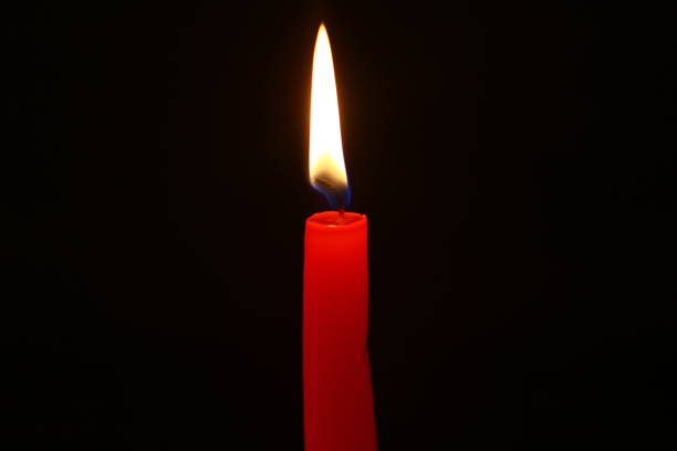 istock single wax lighting red candle with small fire against the black background. 1019849862