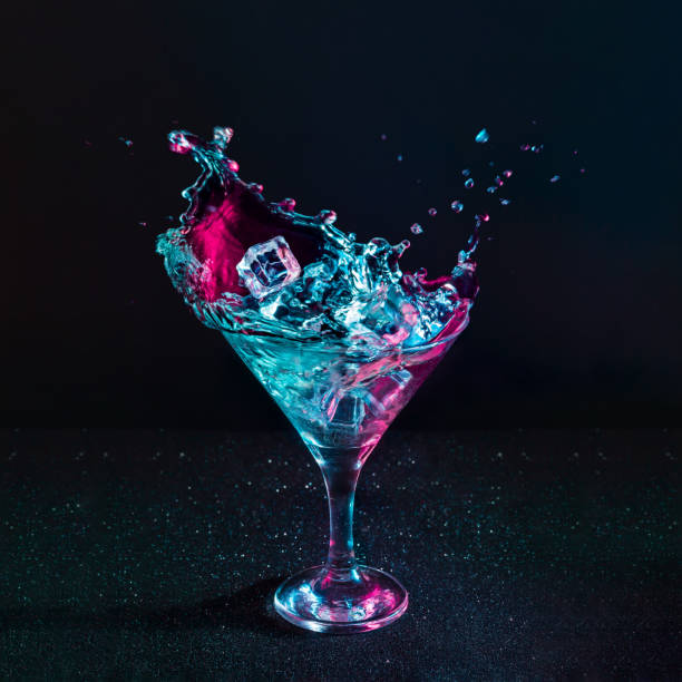 мартини коктейль напиток всплеск с кубиками льда в неоновых радужных розовых и синих цветов. - martini cocktail martini glass glass стоковые фото и изображения