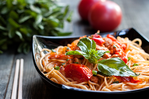 Spaghetti in tomato sauce with chicken, tomatoes, decorated with parsley on a wooden table