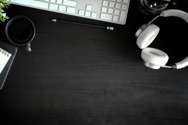 istock Dark desk with desktop computer, headphones, books, pen and a coffee mug. Top view with copy space. 1019858478