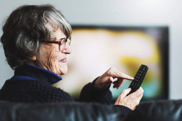 istock Senior woman smiles as she uses TV remote control 1019866634