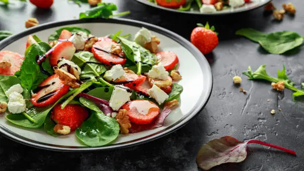 Photo of Summer Fruit Strawberry, spinach Salad with walnut, feta cheese balsamic vinegar, kale. in a plate. concepts health food