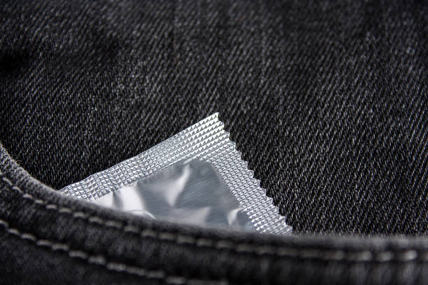 un préservatif est dans la poche avant du jean noir. gros plan. - sex condom jeans horizontal photos et images de collection