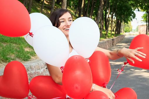 Girl in park with balloons smiling. Red and white colors. Joyful emotions.