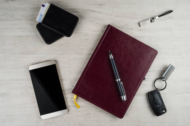 Smartphone, desk pad, ignition key, pen and other men's accessories on the surface with a texture of bleached oak.