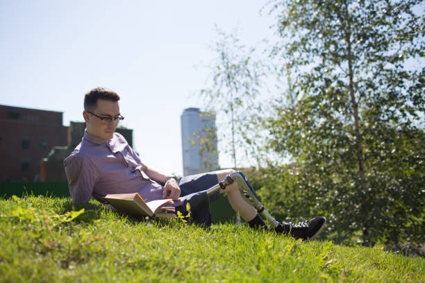 istock Disabled young man with foot prosthesis read book on grass 1019900074