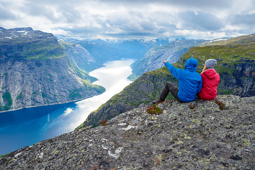 Couple sits on rock and looks at mountains near Trolltunga. Popular tourist attraction. Ringedalsvatnet - lake in the municipality of Odda in Hordaland county, Norway