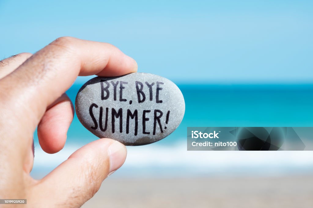 man on the beach and text bye, bye summer closeup of the hand of a young caucasian man on the beach, in front of the ocean, holding a stone with the text bye, bye summer written in it Summer Stock Photo