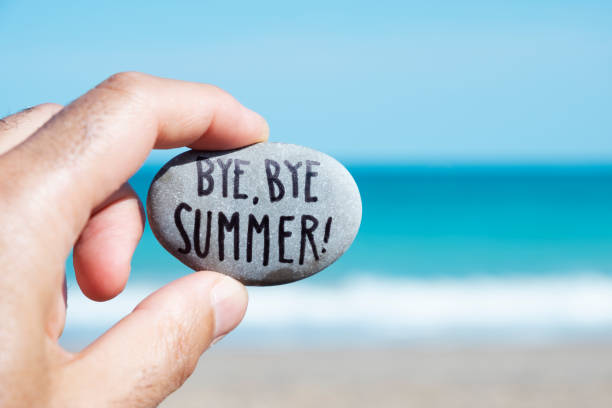 man on the beach and text bye, bye summer closeup of the hand of a young caucasian man on the beach, in front of the ocean, holding a stone with the text bye, bye summer written in it endland stock pictures, royalty-free photos & images