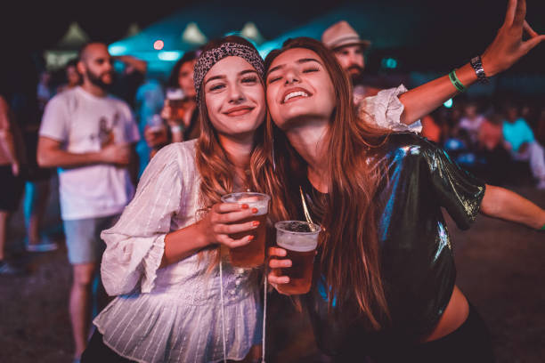 zwei junge frauen, genießen sie eine nacht auf dem musikfestival - festival alcohol stock-fotos und bilder