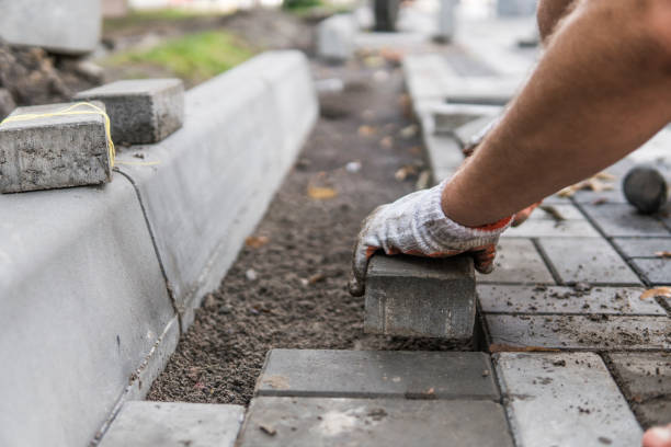 mani di un costruttore nelle sue mani guantate arancioni con un raccordo a martello che posa nuove pietre da pavimentazione esterne posizionandone con cura una posizione su una base di terreno livellata e rastrellata. fondazione di sabbia. edificio. - gloved foto e immagini stock