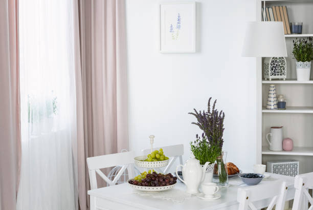 istock Plants on white table in bright dining room interior with poster and pink drapes at window. Real photo 1019945860