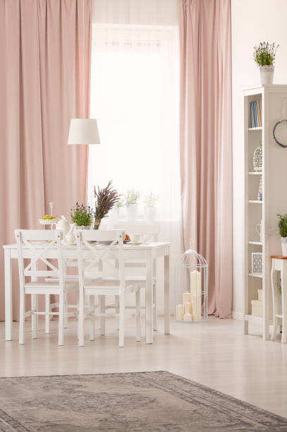 istock White chairs at table with plants in pastel pink dining room interior with rug and drapes. Real photo 1019945876
