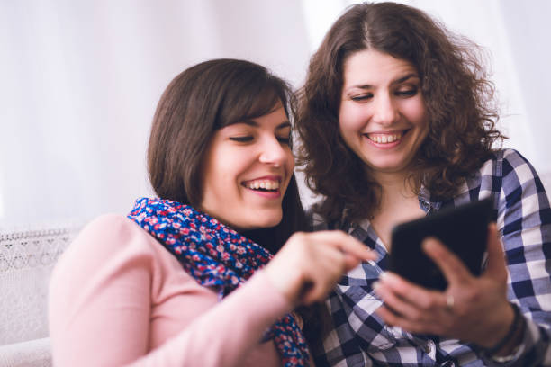 istock Two cheerful woman relaxing indoor and using tablet. 1019954724