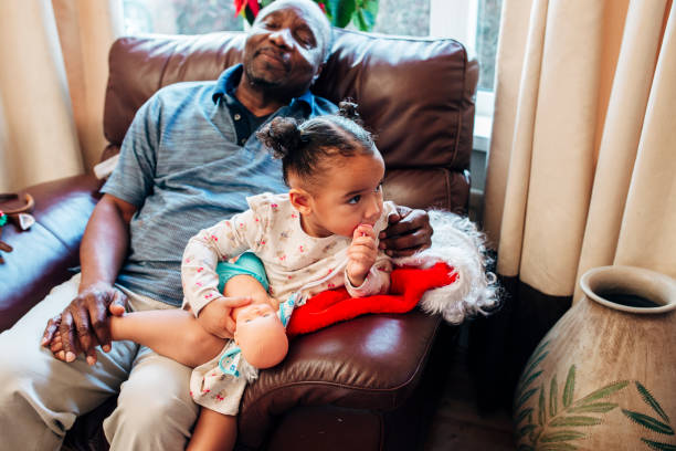 Sitting with her Grandfather at Christmas A little girl sits on the sofa with her grandfather at Christmas as he takes a nap. sleeping grandpa stock pictures, royalty-free photos & images