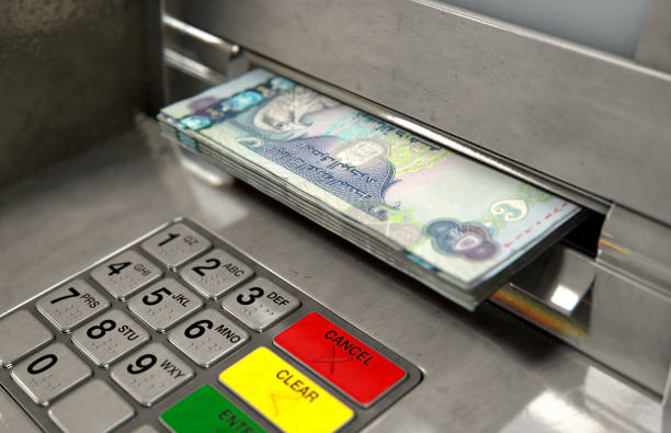 A closeup view of an atm facade with an illuminated sceen and keypad and a wad of dubai dirham banknotes being withdrawn from the cash slot - 3D render