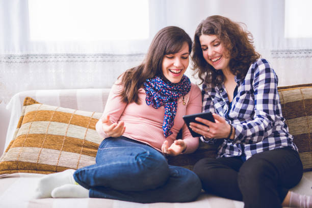istock Two women laughing while sitting on the couch together and looking at the tablet. 1019959200