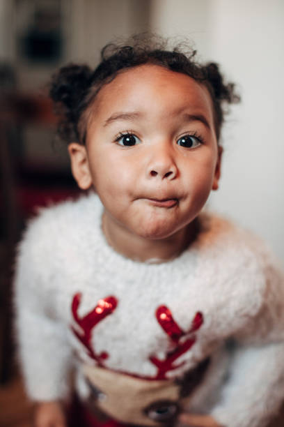 A little girl looks at the camera as she poses for a headshot in a Christmas jumper.