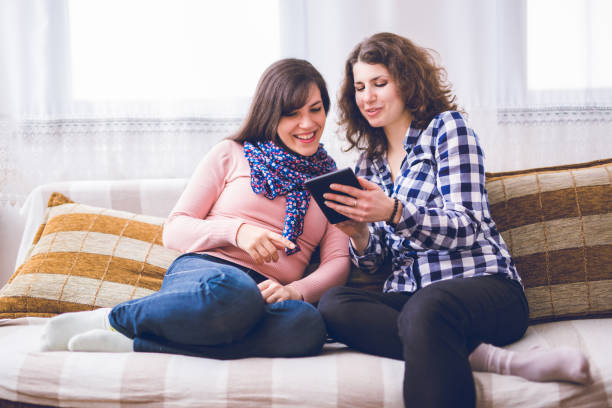 istock Two women laughing while sitting on the couch together and looking at the tablet. 1019961820