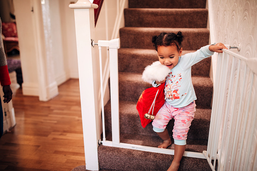 A little girl walks down the stairs on Christmas morning, carrying her stocking about to go see what is left under the tree for her.