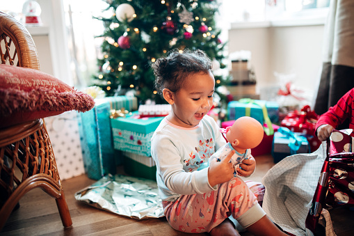 A little girl excitedly looks at a doll she's just received as a gift on Christmas morning.