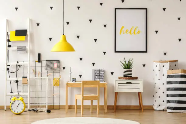 Poster in a black frame on a white wall with stickers in a scandinavian style child bedroom interior with wooden furniture and yellow decorations
